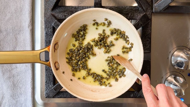 Stirring capers in olive oil in small skillet on stovetop