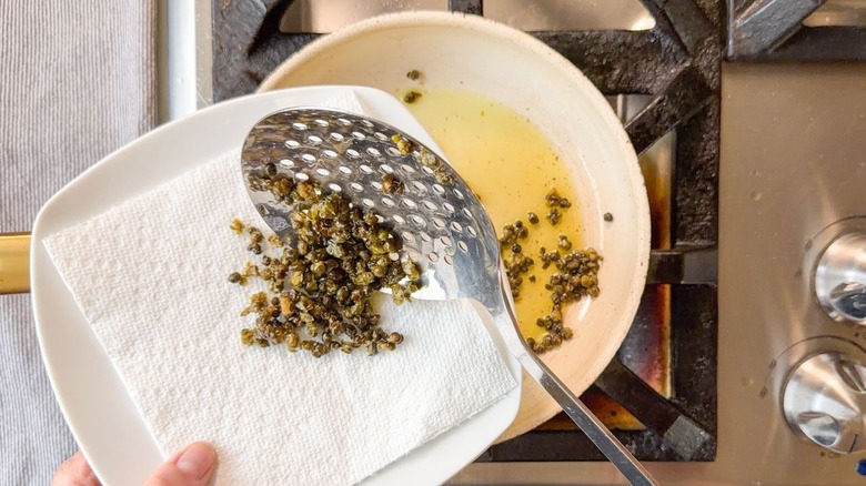 Transferring fried capers from skillet to paper towel-lined plate with slotted spoon