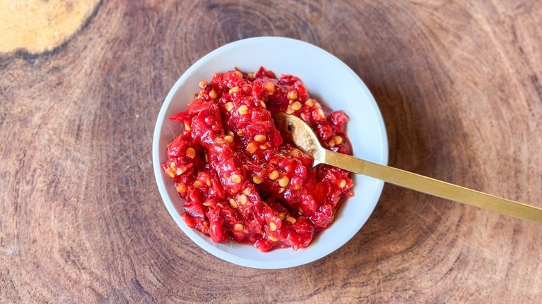 Calabrian chile paste in small bowl on wooden board with gold spoon