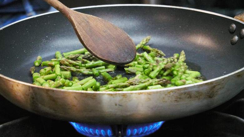 Cooking asparagus in a pan with a wooden spoon