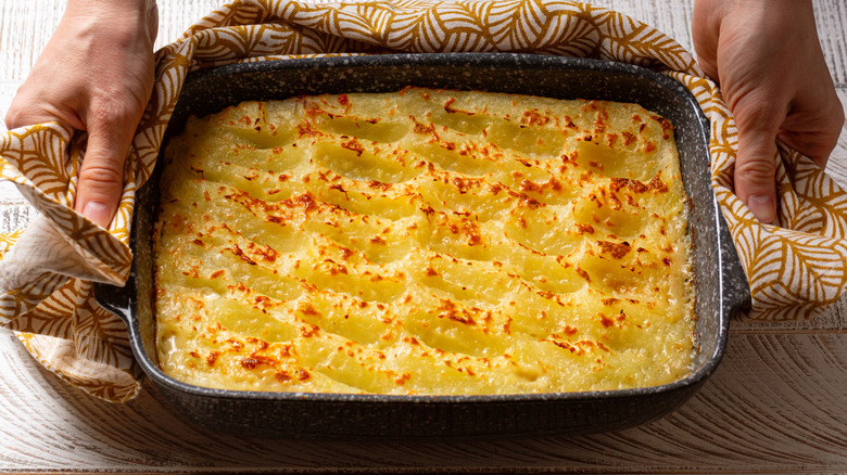A person's hands are seen holding baked shepherd's pie in a dish.