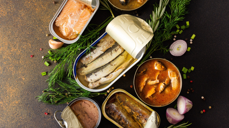 Various open cans of meat on a table beside herbs and raw red onion