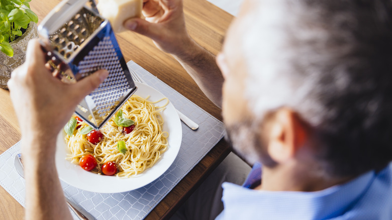 Person grating cheese onto pasta