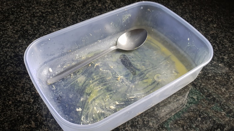 A greasy plastic container with a spoon in it.