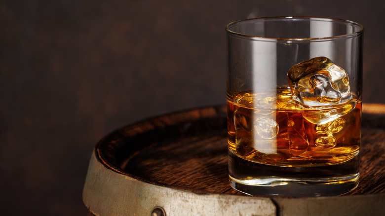 A rocks glass of whiskey sits atop a whiskey barrel.