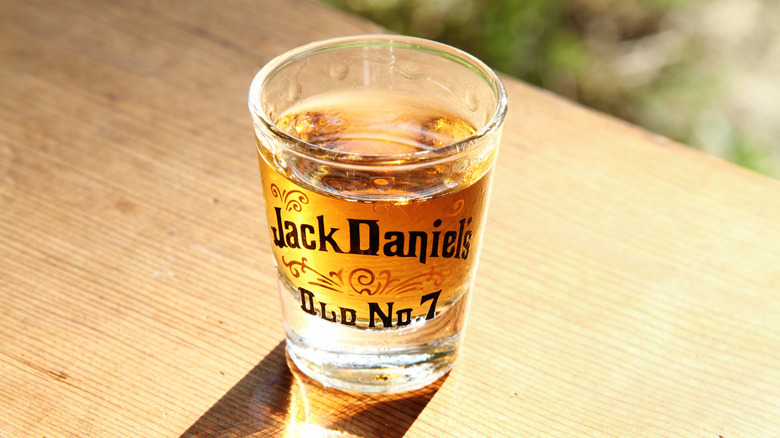 Jack Daniel's shot glass of Old No. & whiskey on wood table in sunlight.