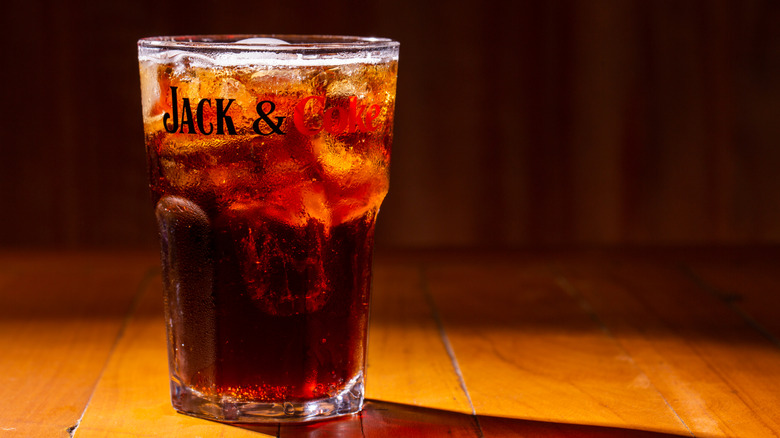 A Jack and Coke in a branded glass on a wooden table.