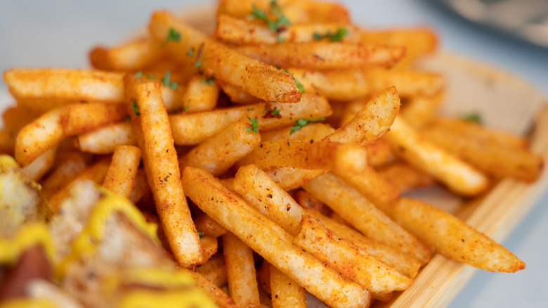Golden crispy seasoned French fries served on a wooden tray, sprinkled with herbs and spices