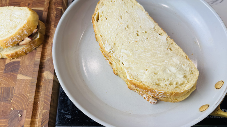 Sandwich in skillet with top bread coated in mayonnaise