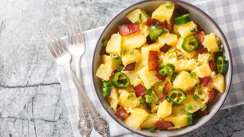A bowl of potato salad with sliced jalapeños, green onions, and chopped bacon