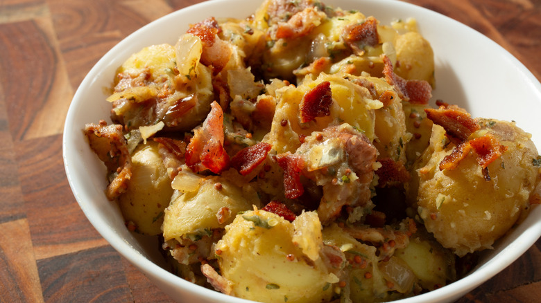 White bowl filled with potato salad with onions and bacon
