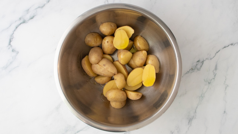 Halved baby potatoes in a large bowl drizzle with olive oil