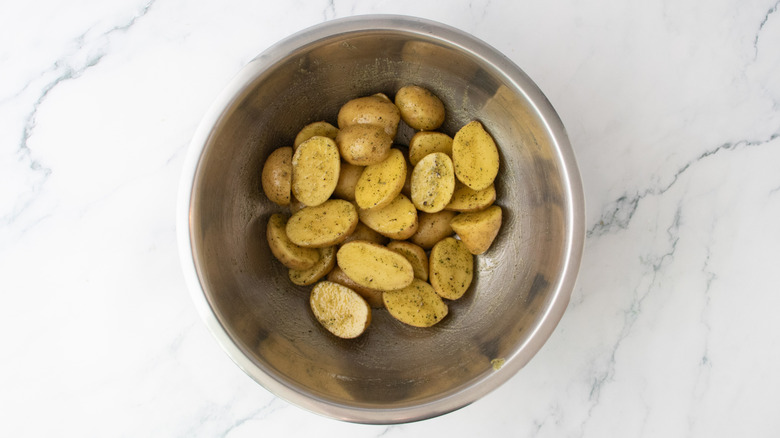 Raw potatoes in a large bowl seasoned with herbs and spices