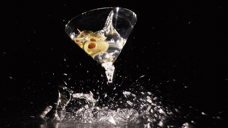 A martini glass shattering into many pieces before a black background