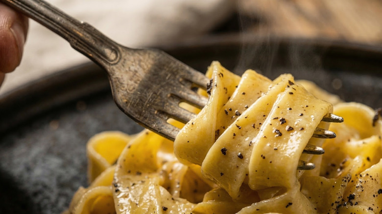 Close-up of a person holding a fork twirled with grated mushroom-laced pasta