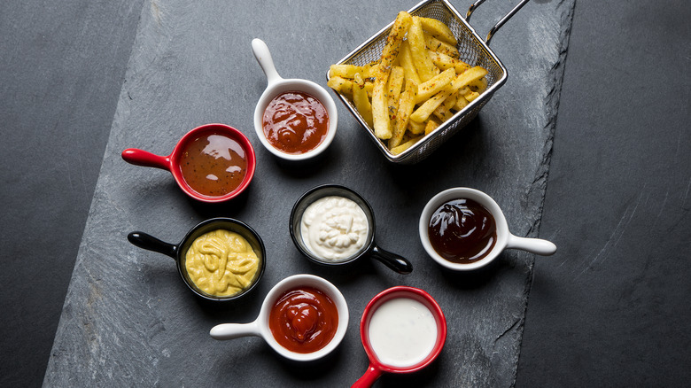 high angle shot of dipping sauces and French fries on a dark surface