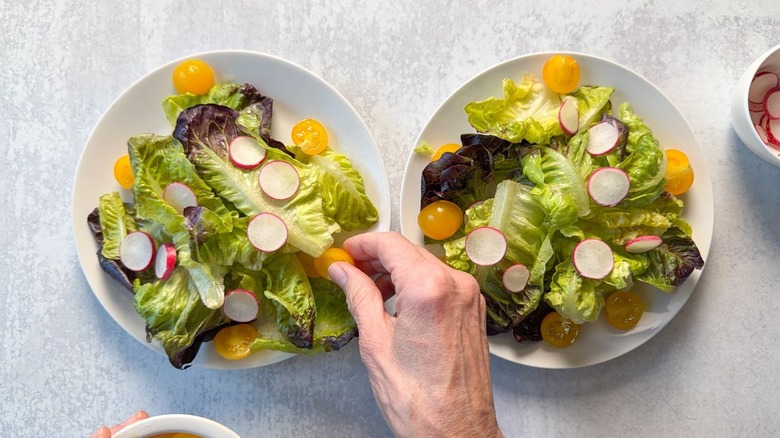 Adding yellow cherry tomatoes and radish slices to little gem lettuce on salad plates