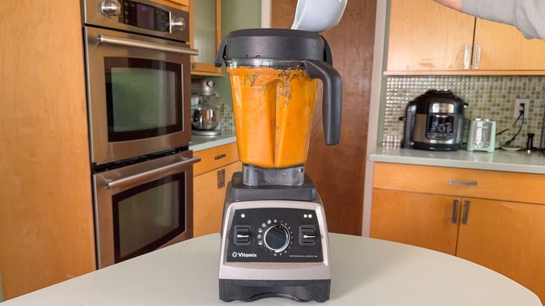 Adding oils to carrot ginger dressing in blender on countertop