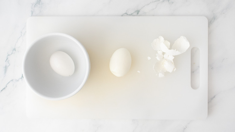 An egg peeling station with eggs in ice water, shells, and a peeled egg.