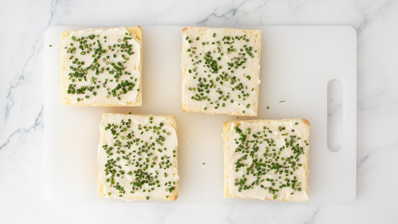 Crustless bread slices spread with softened butter and sprinkled with chives