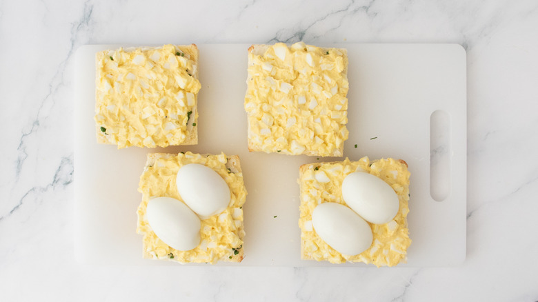 Bread slices topped with egg salad and soft boiled egg halves.