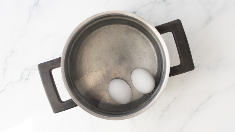 A large saucepan with two eggs covered in water.
