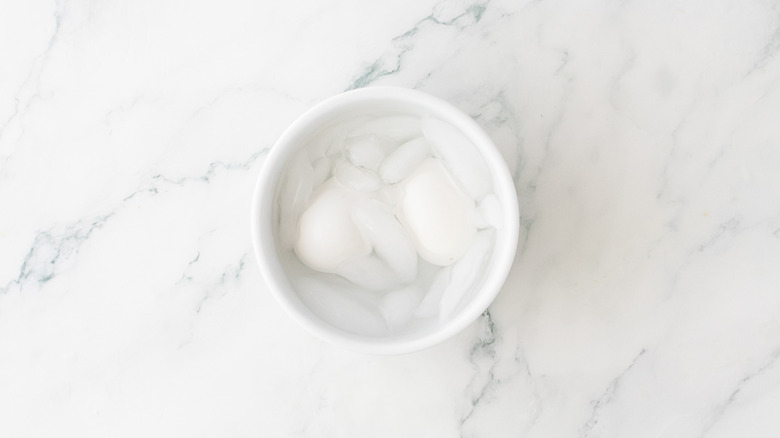 A white bowl with two eggs covered in ice water.