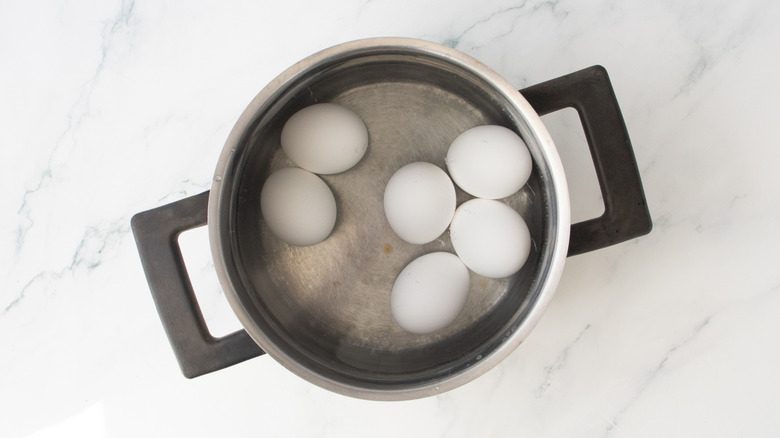 A large saucepan with six eggs covered in water.