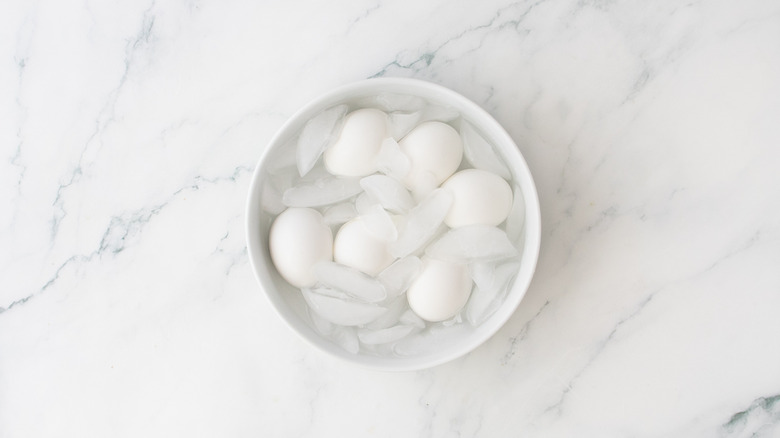 A large white bowl with six eggs covered in ice water.