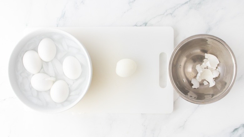 An egg peeling station with eggs in ice water, shells, and a peeled egg.