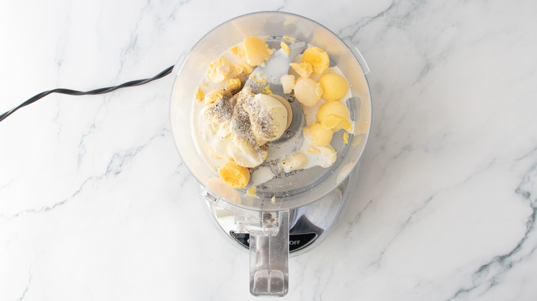 A food processor with hard boiled egg yolks, mayonnaise, and seasoning