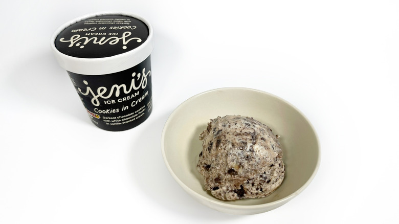 A pint of Jeni's Cookies in Cream next to a bowl with a scoop