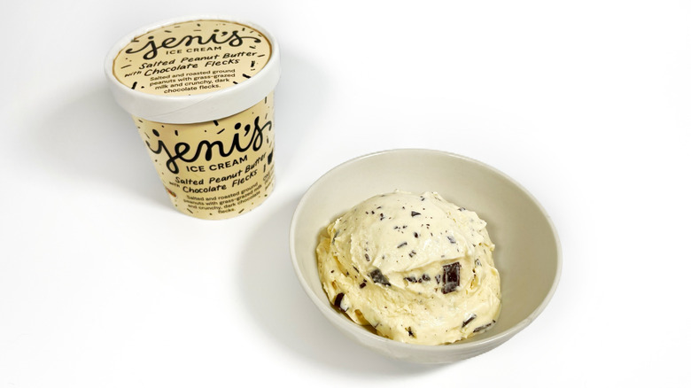 A pint of Jeni's Salted Peanut Butter with Chocolate Flecks next to a bowl with a scoop