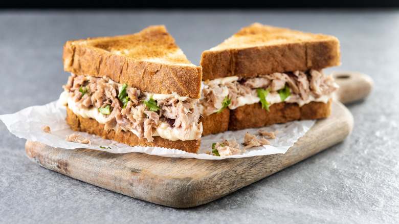 A tuna salad sandwich cut in half on a wooden board