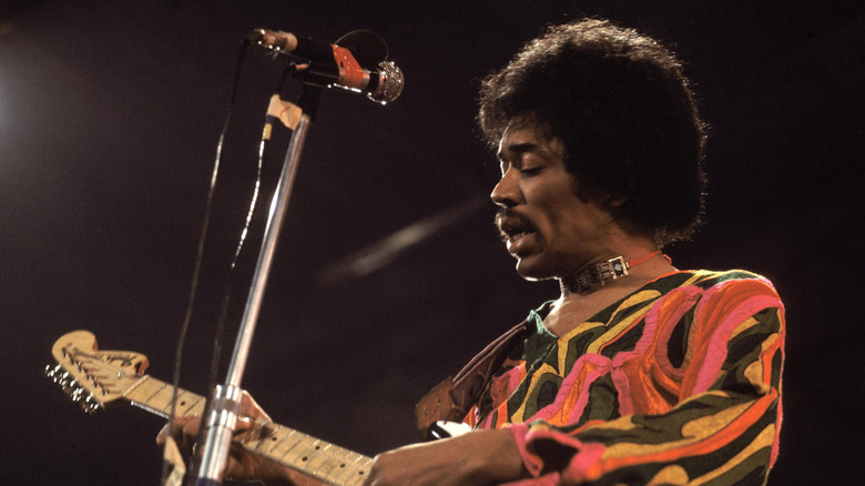 Jimi Hendrix with a guitar, singing into a mic
