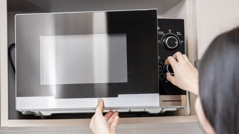 A woman adjusts the settings on a microwave while closing the door