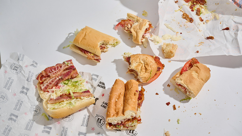 Several different BLT sandwiches with bites taken out of them on a table