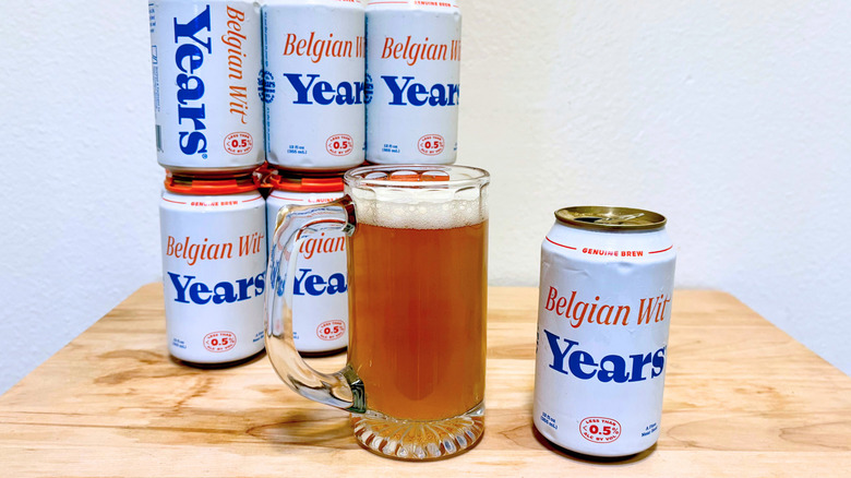 A stein of Years Belgian Wit next to its can, with more cans in the background