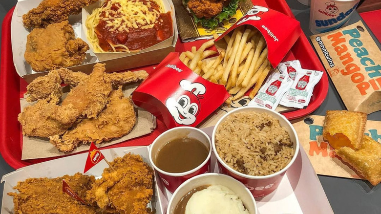 A table covered with lots of Jollibee menu items including Chickenjoy fried chicken, spaghetti, rice, pies, and more