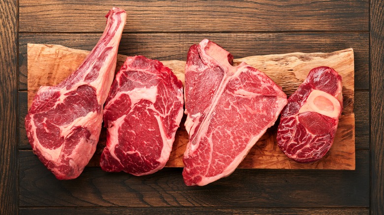 Raw steaks on wooden cutting board.