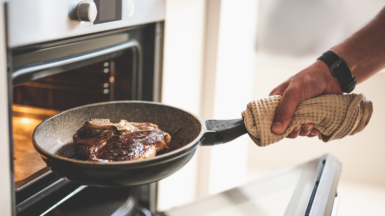 A steak in a pan being taken out of an oven.