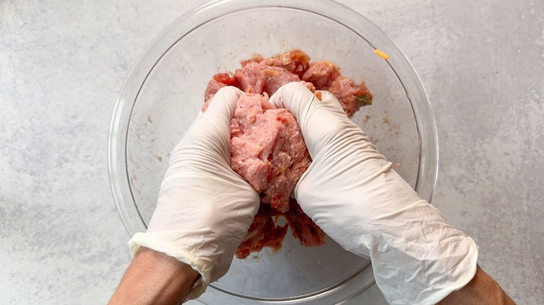 Mixing juicy 3-ingredient tex-mex turkey burgers by hand with gloves in glass bowl