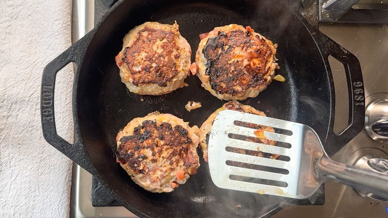 Flipping juicy 3-ingredient tex-mex turkey burgers with metal spatula in cast iron skillet