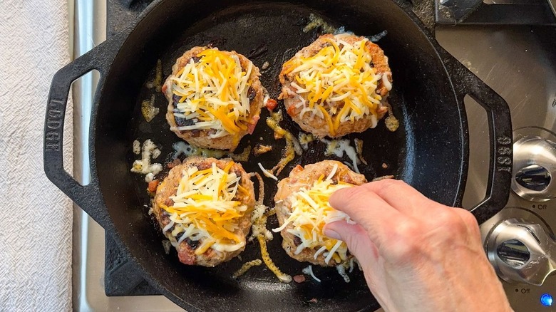 Juicy 3-ingredient tex-mex turkey burgers topped with shredded cheese in cast iron skillet on stovetop