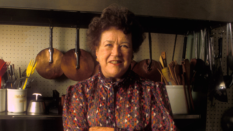 Julia Chiild appears at a table abundant with produce and wine bottles.
