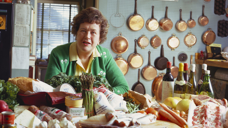 Celebrity chef Julia Child is photographed at a table full of ingredients in a cozy kitchen.