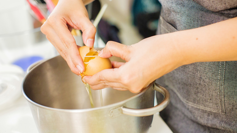 a woman cracks an egg into a mixing bowl