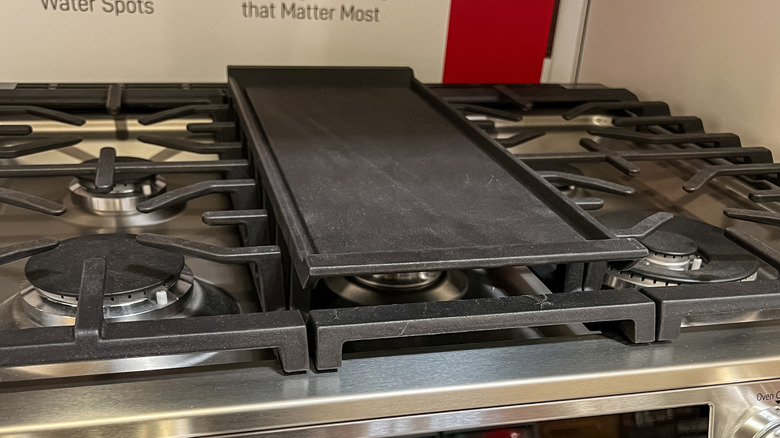 A kitchen stove grilltop between two sets of burners on either side.
