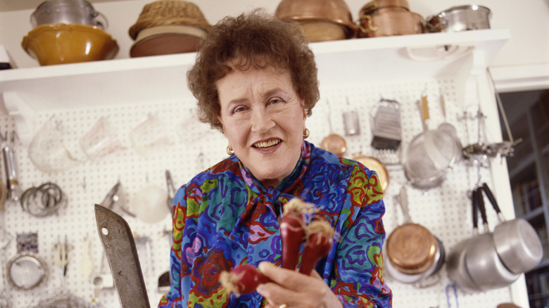 Julia Child smiling and holding a knife and vegetables