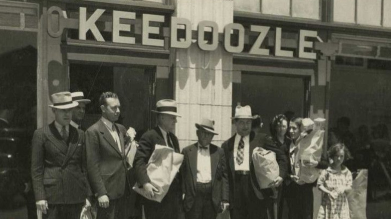 Black and white photo: people stand in front of Keedoozle.